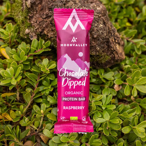Moonvalley Bio-Proteinriegel mit Himbeere und Schokoladenüberzug, fotografiert in einer natürlichen Outdoor-Umgebung.