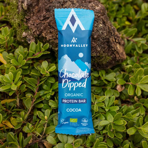 Moonvalley Bio-Proteinriegel mit Kakao und Schokoladenüberzug, fotografiert in einer natürlichen Outdoor-Umgebung.