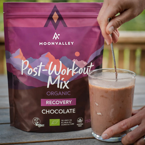 Ein Glas fertig gemischtes Schokoladengetränk aus dem Moonvalley Post-Workout Mix wird mit einem Löffel umgerührt.